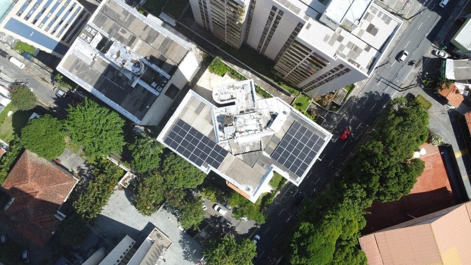 Vista aérea de quadra residencial com painéis solares no telhado, obra da Otimize