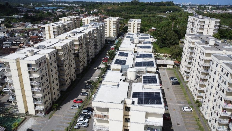 Condomínio de blocos altos com painéis solares nas coberturas e o mar ao fundo