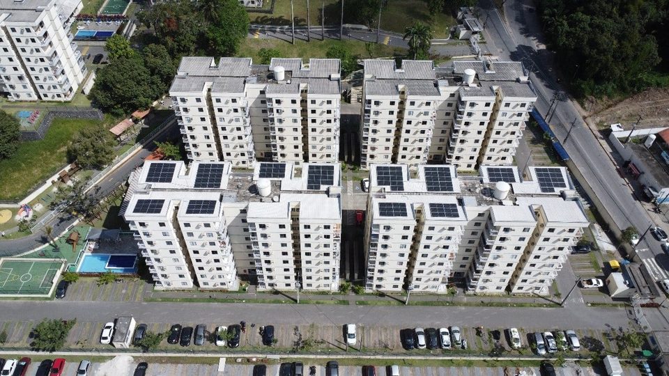 Condomínio de cinco blocos brancos com painéis solares em todas as coberturas