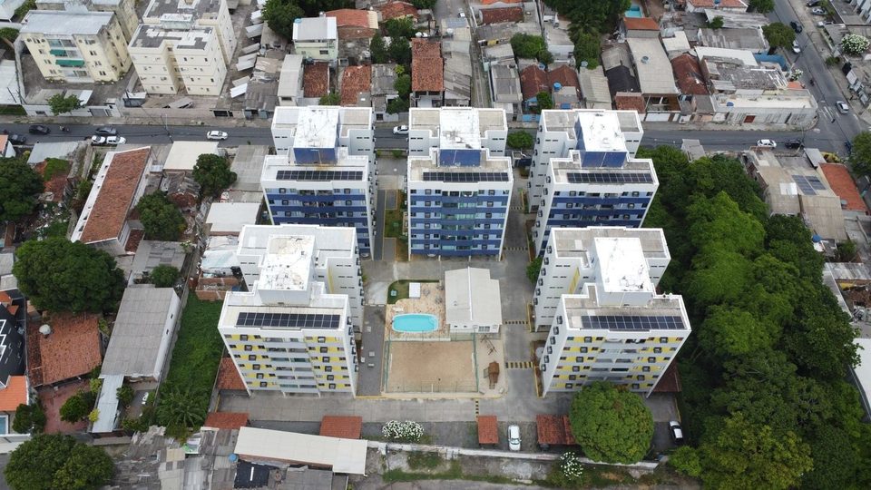 Vista aérea de condomínio com piscina e três blocos com painéis solares nas coberturas
